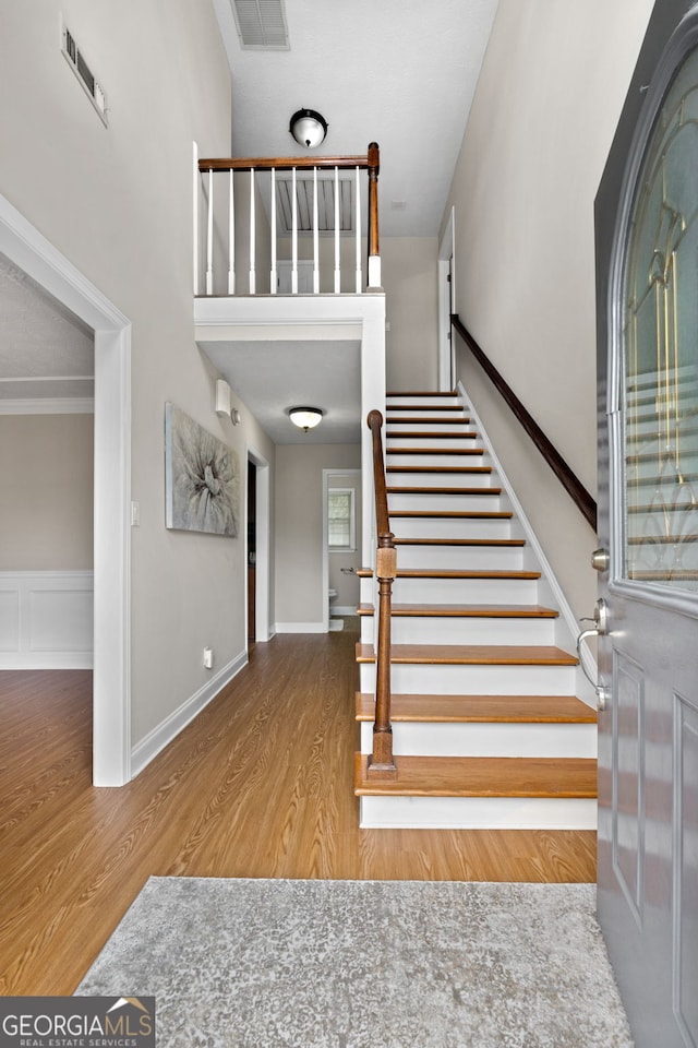 entryway featuring stairway, a towering ceiling, wood finished floors, and visible vents