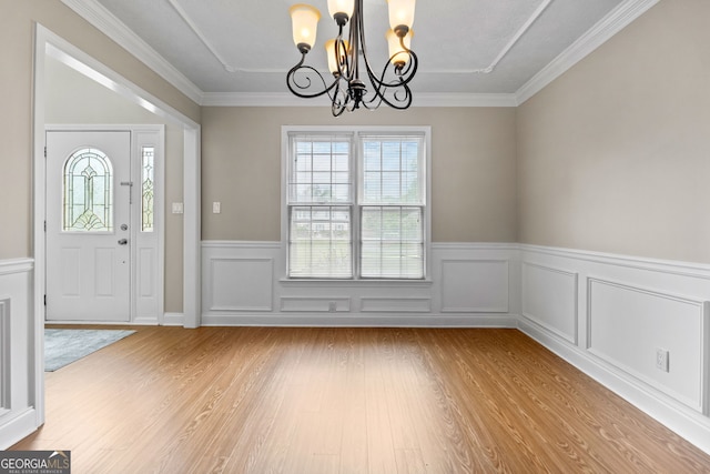 entrance foyer featuring ornamental molding, a chandelier, wainscoting, and light wood-style flooring