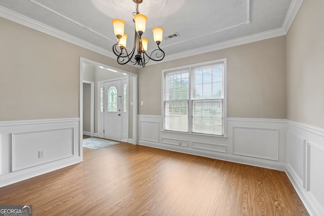 unfurnished dining area with visible vents, crown molding, wainscoting, an inviting chandelier, and wood finished floors