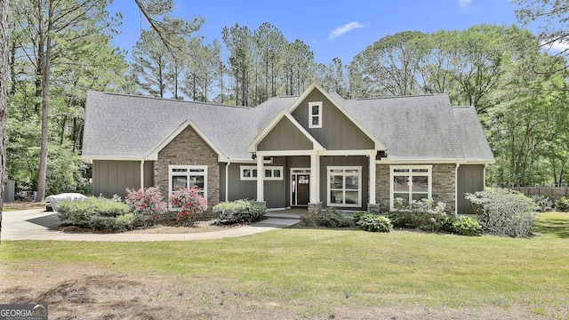 craftsman house with a shingled roof, a front lawn, board and batten siding, and stone siding