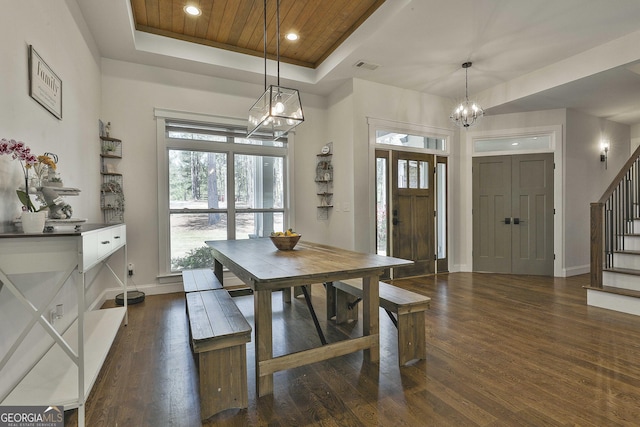 dining room with dark wood-style flooring, stairs, a tray ceiling, and a notable chandelier
