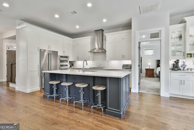 kitchen with wall chimney range hood, stainless steel appliances, visible vents, and a sink