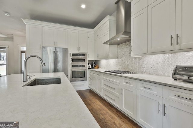 kitchen featuring a sink, appliances with stainless steel finishes, tasteful backsplash, and wall chimney exhaust hood