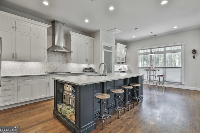 kitchen featuring a sink, light countertops, an island with sink, wall chimney exhaust hood, and white cabinetry