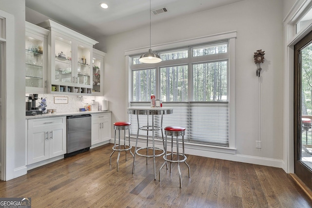 bar featuring backsplash, wet bar, stainless steel dishwasher, baseboards, and dark wood-style floors