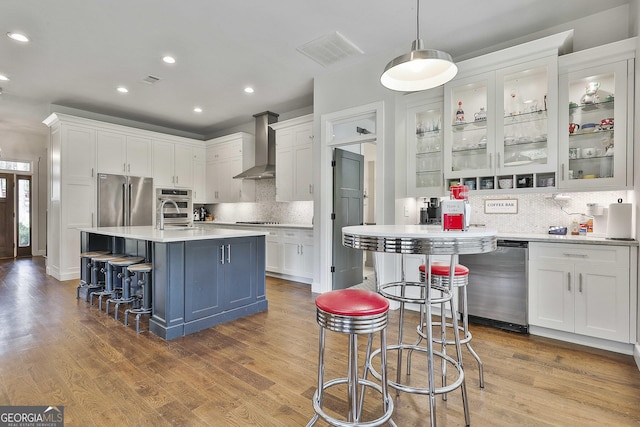 kitchen featuring visible vents, wall chimney range hood, white cabinetry, tasteful backsplash, and stainless steel appliances