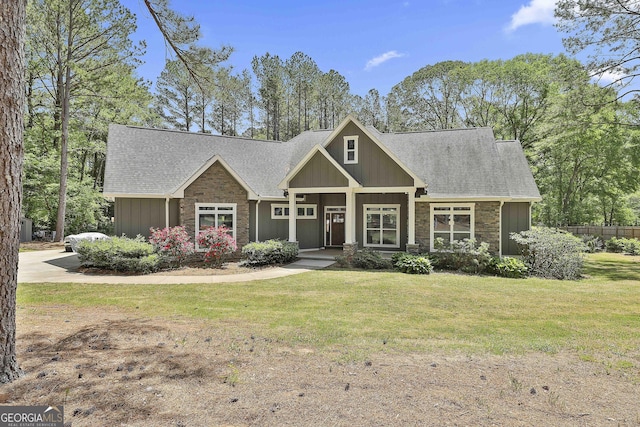 craftsman-style home with board and batten siding, roof with shingles, a front yard, and stone siding