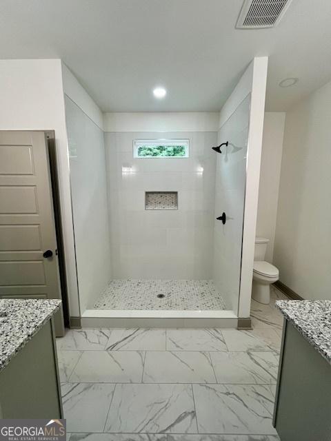 bathroom featuring visible vents, marble finish floor, tiled shower, and vanity