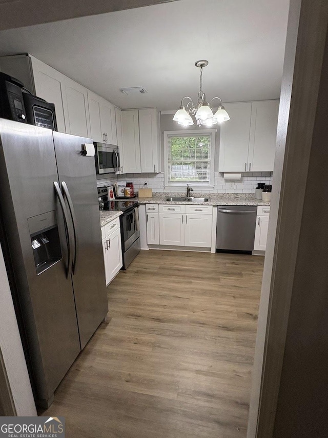kitchen with decorative backsplash, appliances with stainless steel finishes, a sink, a notable chandelier, and white cabinetry
