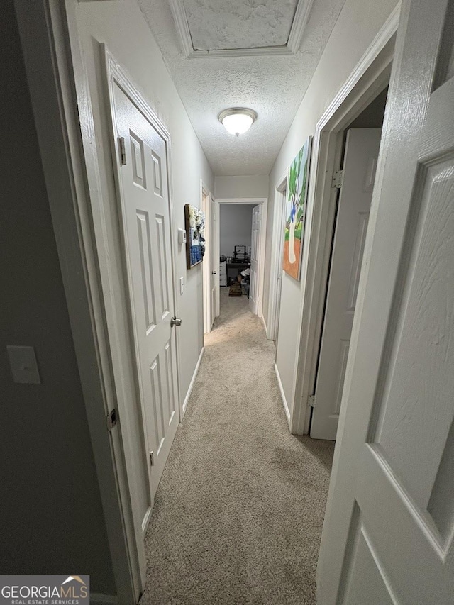 hallway with a textured ceiling and light colored carpet