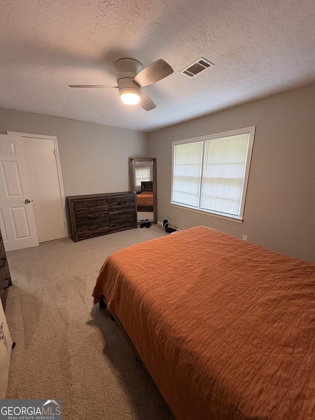 bedroom featuring carpet floors, a ceiling fan, a textured ceiling, and visible vents