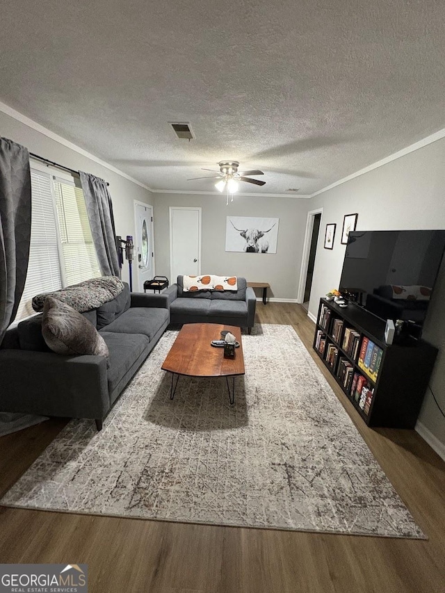 living room with crown molding, a ceiling fan, wood finished floors, and visible vents