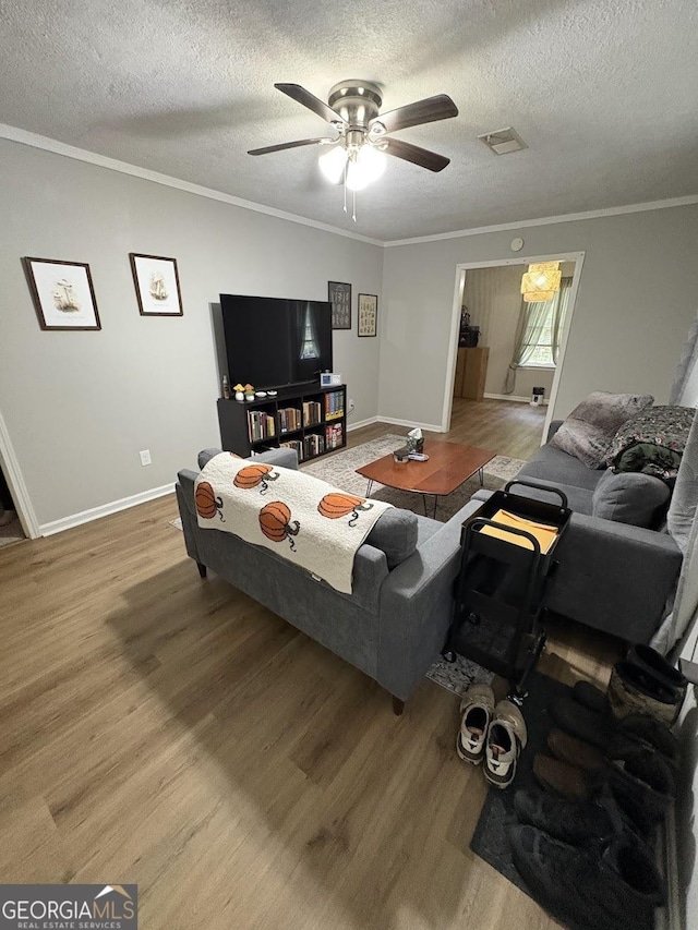 living area with ceiling fan, visible vents, wood finished floors, baseboards, and ornamental molding