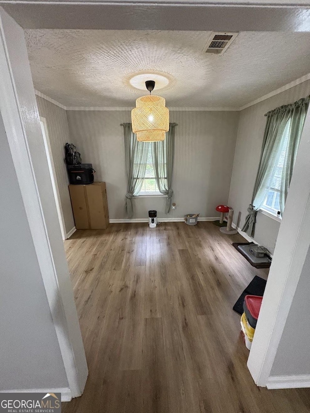 unfurnished dining area with crown molding, a textured ceiling, baseboards, and wood finished floors