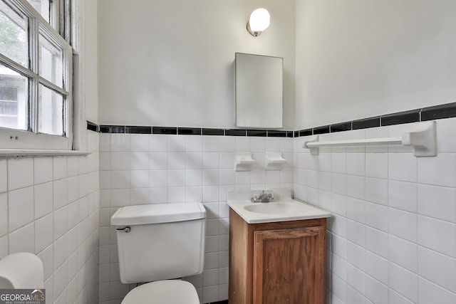 half bathroom with vanity, toilet, tile walls, and a wainscoted wall