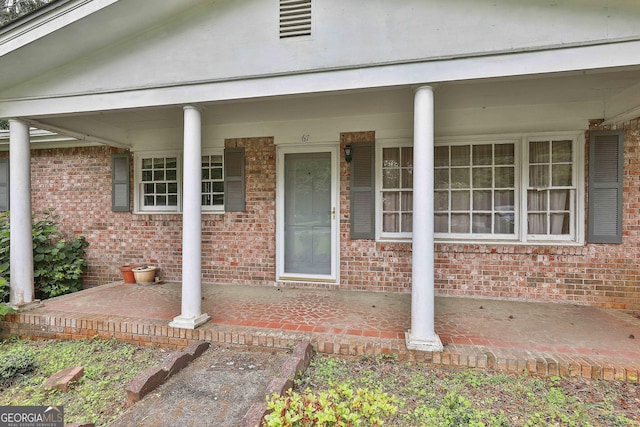 property entrance with brick siding, visible vents, and covered porch