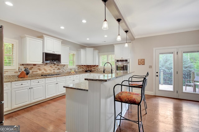kitchen with backsplash, stainless steel appliances, white cabinets, and light wood finished floors