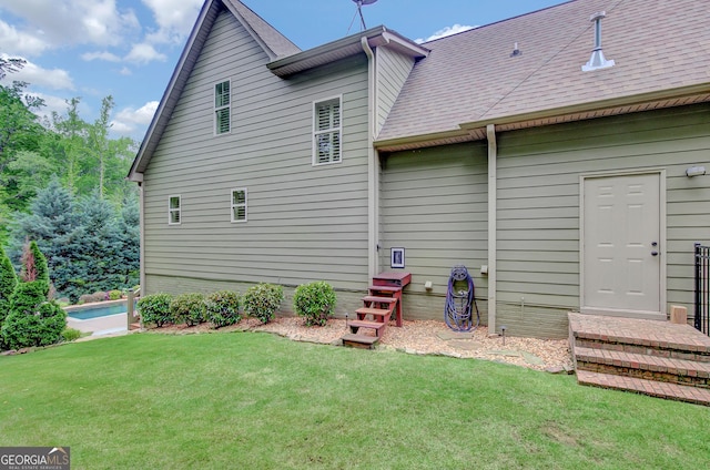 rear view of house featuring a lawn and roof with shingles