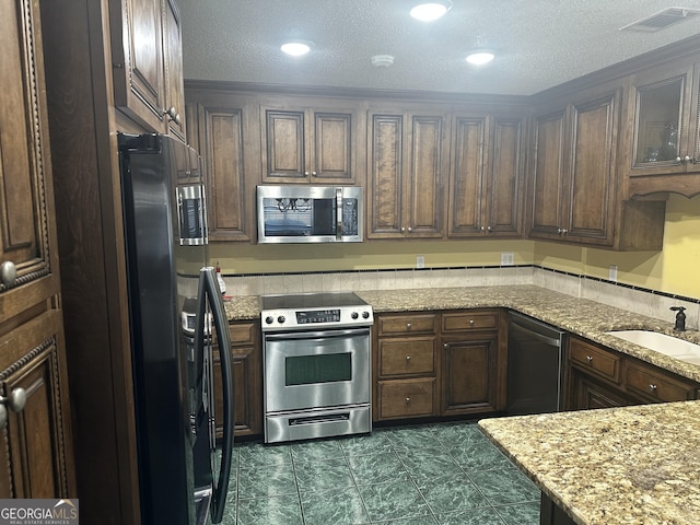 kitchen with visible vents, a textured ceiling, light stone counters, a sink, and appliances with stainless steel finishes