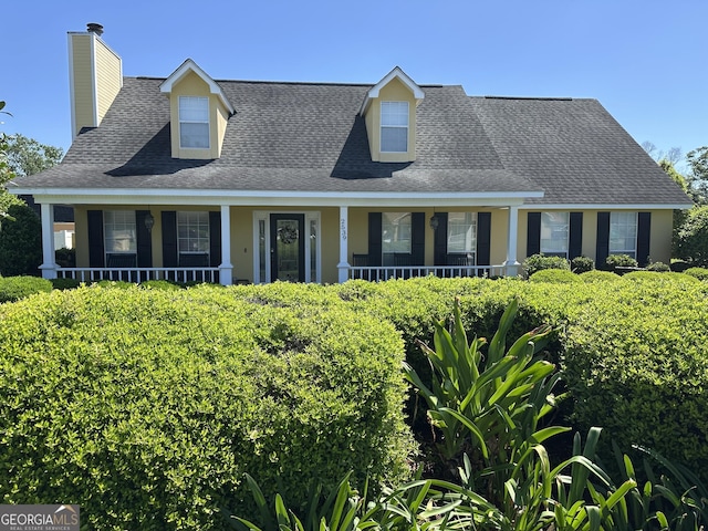 cape cod house featuring a shingled roof, a chimney, and a porch