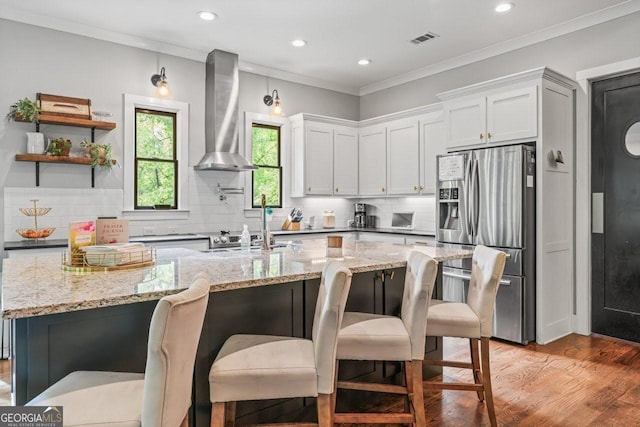 kitchen with visible vents, stainless steel fridge, wall chimney exhaust hood, and tasteful backsplash