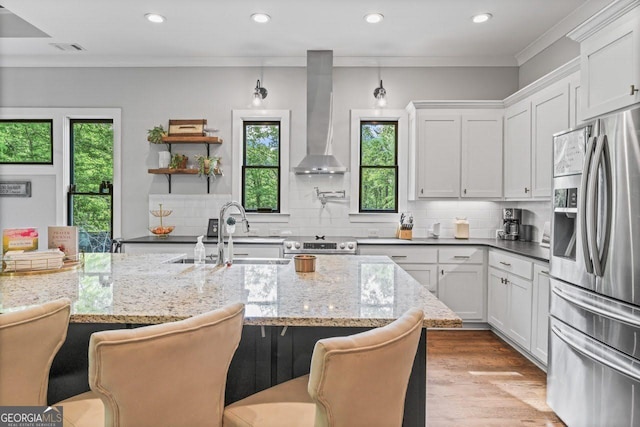 kitchen featuring wall chimney range hood, stainless steel appliances, plenty of natural light, and a sink