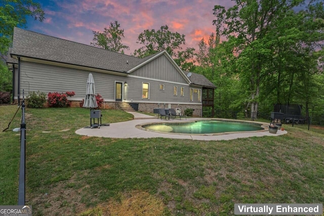 back of house at dusk with a patio, board and batten siding, an outdoor pool, and a yard