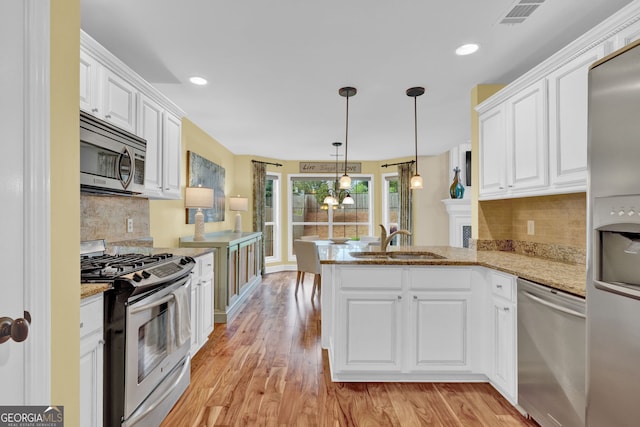 kitchen with a sink, a peninsula, stainless steel appliances, white cabinetry, and light wood-style floors