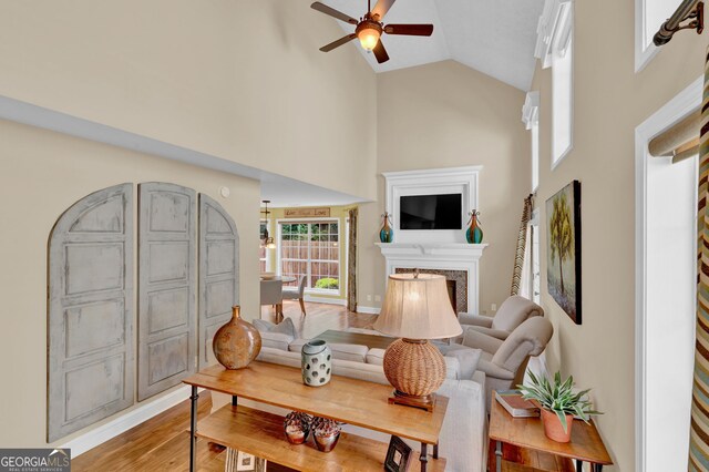 living room with a high end fireplace, light wood-style floors, ceiling fan with notable chandelier, and high vaulted ceiling