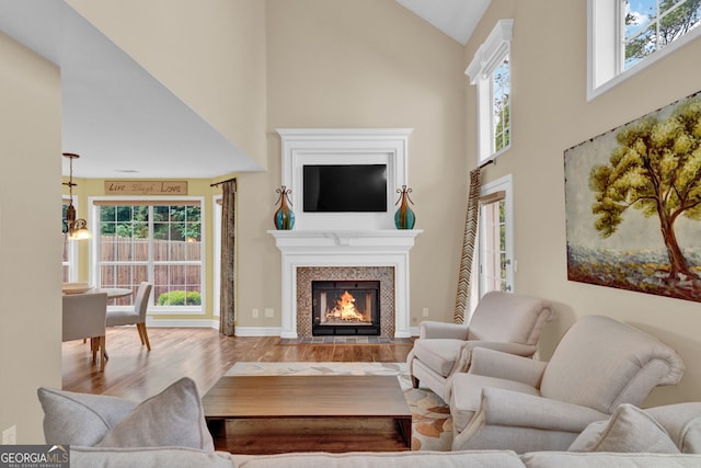 living room featuring baseboards, a tile fireplace, high vaulted ceiling, and wood finished floors