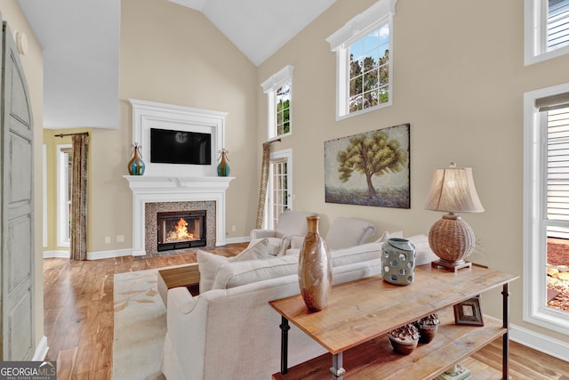 living room featuring baseboards, light wood-style floors, high vaulted ceiling, and a fireplace with flush hearth