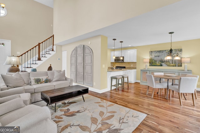 living area with a towering ceiling, stairway, a chandelier, baseboards, and light wood-style floors
