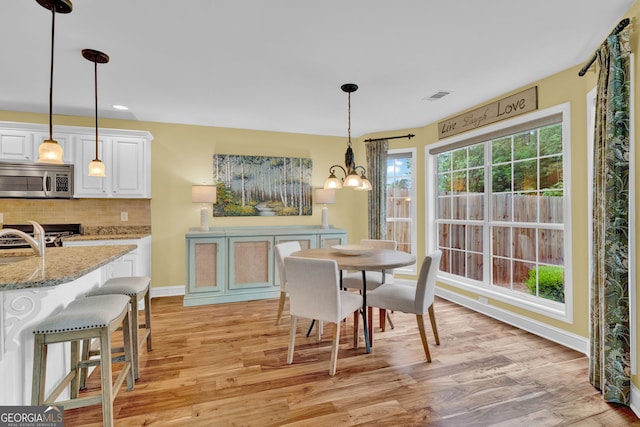 dining space with a chandelier, light wood-style flooring, baseboards, and visible vents