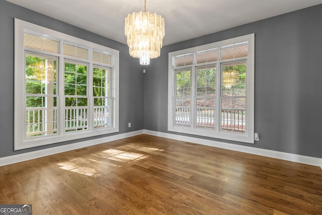 unfurnished dining area with an inviting chandelier, baseboards, plenty of natural light, and wood finished floors