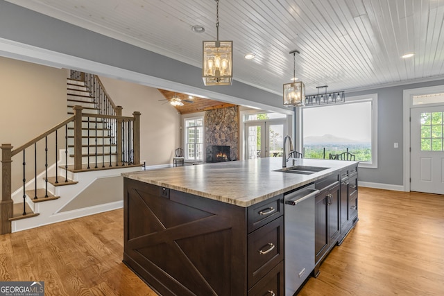 kitchen featuring a kitchen island with sink, pendant lighting, dishwasher, a sink, and light wood-style floors
