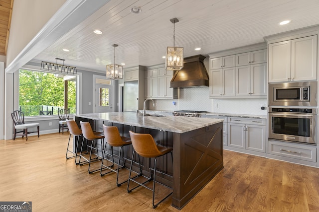 kitchen featuring a notable chandelier, light stone counters, light wood-style floors, stainless steel appliances, and custom exhaust hood