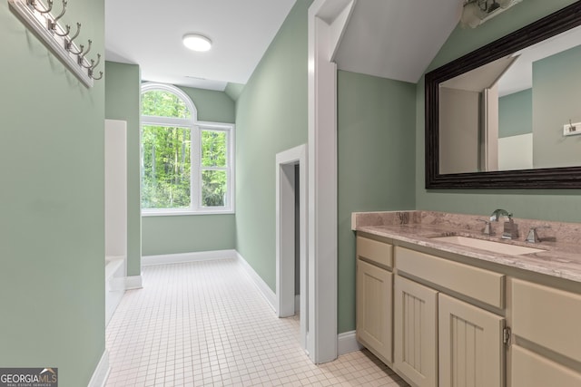 bathroom featuring tile patterned flooring, vanity, baseboards, vaulted ceiling, and a bath