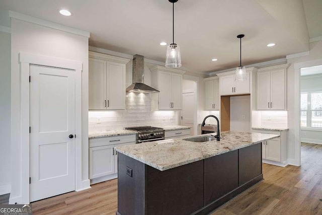 kitchen with wall chimney range hood, a sink, light wood finished floors, and high end stainless steel range oven