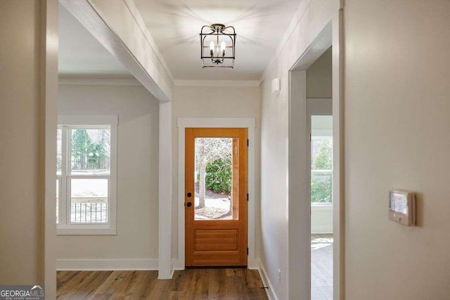 foyer entrance featuring baseboards, ornamental molding, wood finished floors, and a chandelier