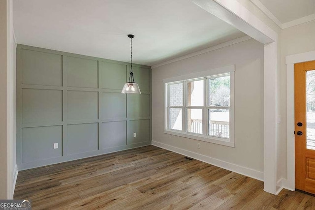 unfurnished dining area with crown molding, baseboards, wood finished floors, and a decorative wall