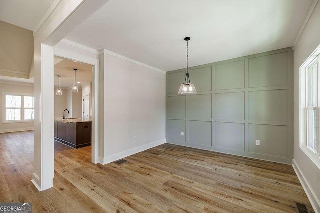 unfurnished dining area featuring a sink, a decorative wall, baseboards, wood finished floors, and ornamental molding