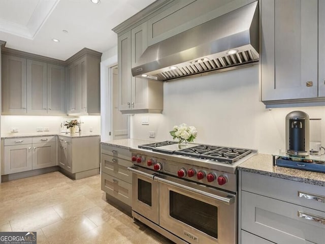 kitchen featuring wall chimney range hood, gray cabinets, range with two ovens, light stone counters, and recessed lighting
