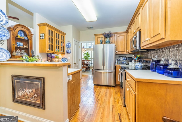 kitchen featuring stainless steel appliances, light wood finished floors, glass insert cabinets, light countertops, and a peninsula