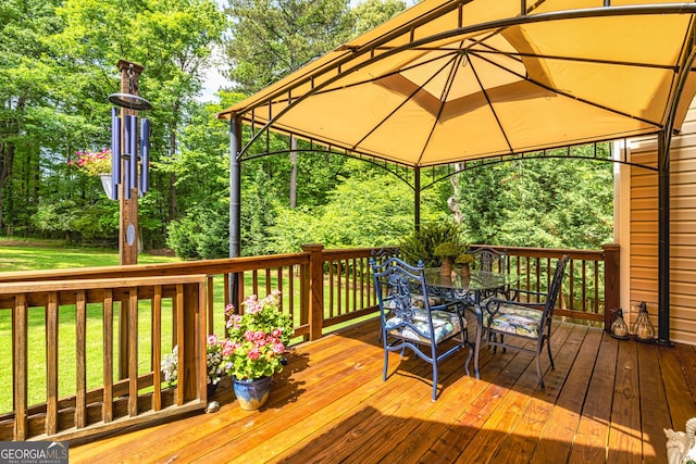 deck with a gazebo, outdoor dining area, a yard, and view of wooded area