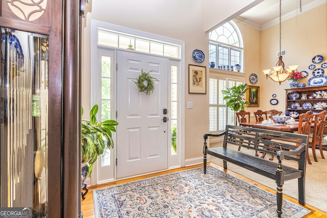 entryway featuring a chandelier, light wood-type flooring, ornamental molding, healthy amount of natural light, and a high ceiling