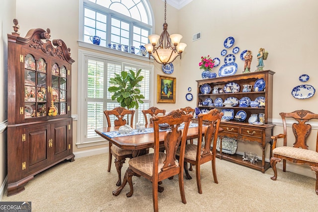 dining space featuring a chandelier, light carpet, crown molding, and a high ceiling