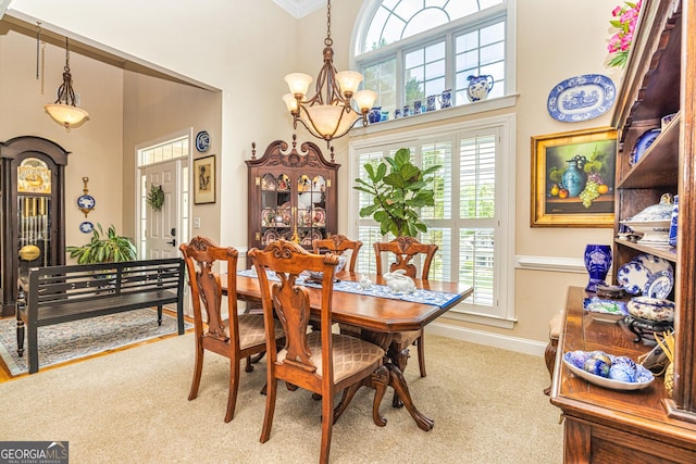 dining area featuring a chandelier, healthy amount of natural light, carpet flooring, a towering ceiling, and ornamental molding