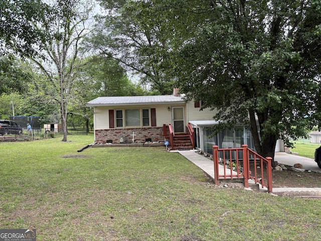 tri-level home featuring a chimney, metal roof, a front yard, brick siding, and fence