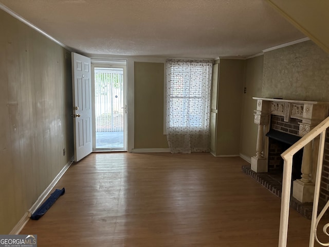 unfurnished living room with crown molding, baseboards, a brick fireplace, and wood finished floors