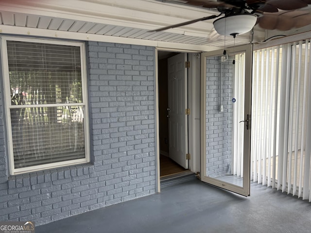 view of exterior entry with ceiling fan and brick siding